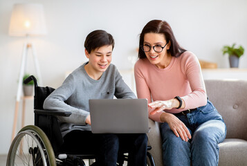 Home schooling concept. Disabled teen boy in wheelchair studying new online materials together with...