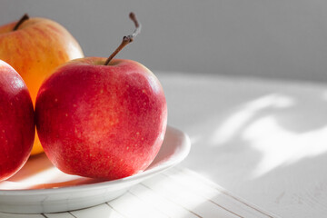 Red apple close up in a white bowl on a white table.