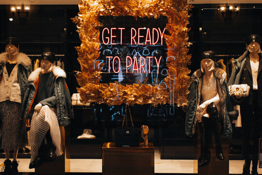 Neon shiny holiday signboard on boutique showcase with text Get ready for party and female mannequins