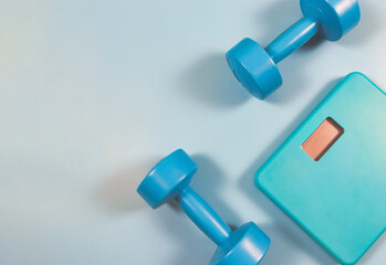 flat lay of blue weight scale and blue dumbbells on blue background with copy space. Sports and weight loss concept.