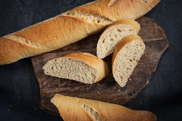 Half sliced baguette on dark rustic wood. dark background. Top view.