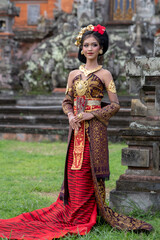 Beautiful balinese girl in traditional costume with a flower and a crown in her hair, and local temple
