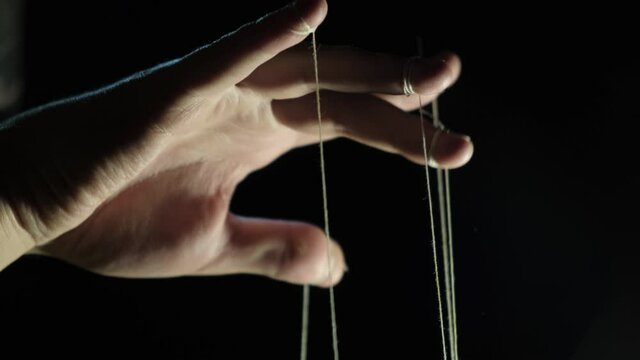 The puppeteer's hand controls the puppets on strings. Manipulation concept