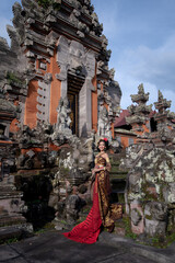 Beautiful balinese girl in traditional costume with a flower and a crown in her hair, and local temple