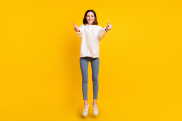 Photo of reliable active lady jump raise thumb up wear white hoodie jeans shoes isolated yellow...