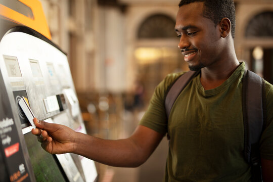 Smiling African Man Using ATM Machine. Happy Young Man Withdrawing Money From Credit Card At ATM.