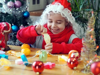 Fototapeta na wymiar A little girl wearing a Santa Claus hat eats tangerines. The eve of the meeting of Christmas.