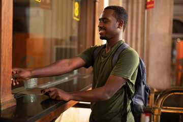 Young man buying a ticket for train with a credit card. Handsome smiling man going to a trip..