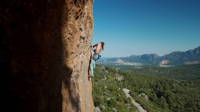 muscular man rock climber in bright blue pants climbing the challenging route on the cliff in Turkey. strong attractive rock climber climbs on a rocky limestone wall, side view. sport and active