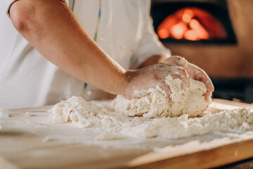 Fototapeta premium The cook prepares the pizza dough. A man kneads the dough with his hands for making pizza in the oven.