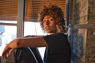 Beautiful woman sitting on the edge of a large window in her studio while making different expressions of joy and depression. Concept of different moods.