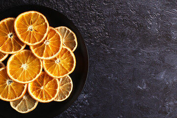 dried slices of orange and lemon fruit on a plate on a dark background with a copy space