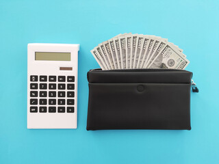 Calculator with dollar banknotes in black wallet on blue background