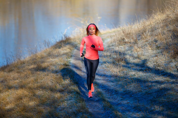 Fitness girl jogging in park near pond in the frosty morning. Running woman training near the lake...