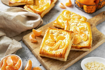 Mini puff pie with cheese cream, almonds, and tangerines on the serving board on the kitchen table. Delicious layered square with citrus fruits, dorblue or ricotta, nuts on a culinary background	