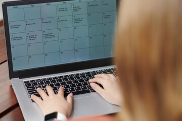 Female entrepreneur filling calendar on laptop, view over the shoulder