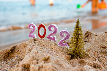 Figures 2022 against background of coastal waves by ocean or sea with caramel cane. Travel during...