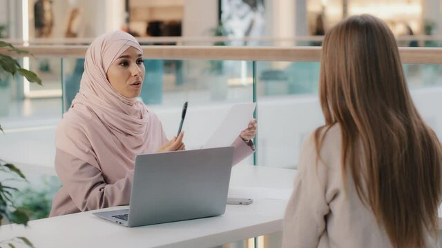 Two young girls sitting at table friendly muslim woman financial advisor explaining benefits contract manager sales agent lawyer consults with client business meeting legal consultation negotiation