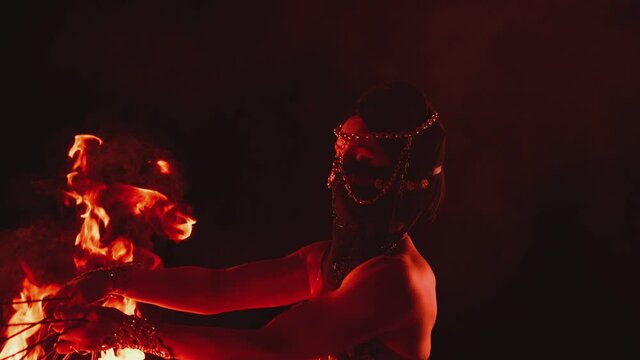 Young woman dancing performing cool and dangerous fire show and doing many tricks with fire . Dressed in black with mask closed half of face . Burning iron fire wings at night. Asian , Arabian culture