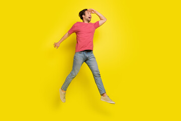 Full size photo of impressed brunet millennial guy jump wear red t-shirt jeans sneakers isolated on yellow background