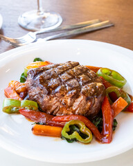 Sliced grilled meat barbecue steak with vegetables on white plate.