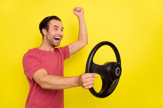 Photo of astonished driver hold steering wheel raise fist rejoice wear pink t-shirt isolated yellow color background