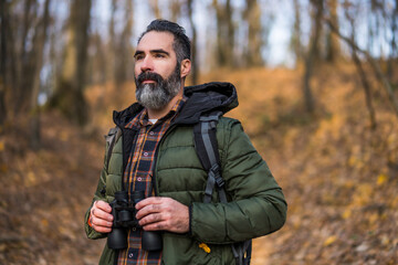Obraz premium Image of man holding binoculars and looking at direction while hiking.
