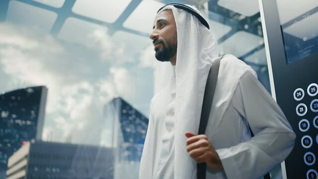 Successful Happy Muslim Businessman in Traditional White Kandura Riding Glass Elevator to Office in Modern Business Center. Saudi, Emirati, Arab Businessman Concept.