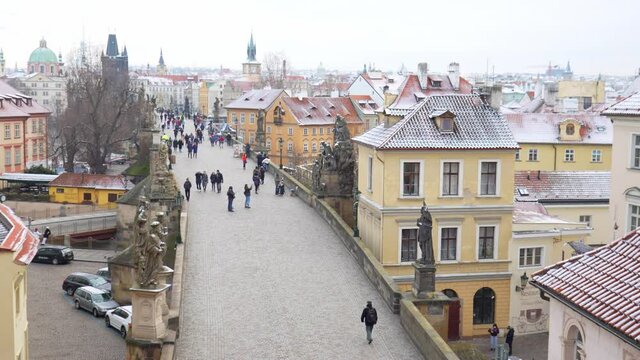 People are walking on Charles bridge, whose rooftops are covered by snow, Prague in the winter