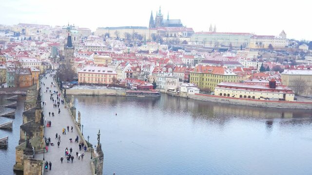 People are walking on Charles bridge, whose rooftops are covered by snow, Prague in the winter