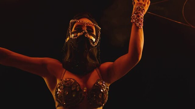 Young woman dancing performing cool and dangerous fire show and doing many tricks with fire . Dressed in black with mask closed half of face . Burning iron fire wings at night. Asian , Arabian culture
