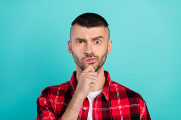 Photo of unsure young brunet guy hand chin wear red shirt isolated on teal color background