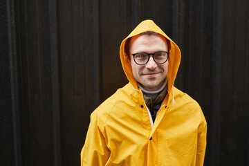 Horizontal medium close-up shot of Caucasian man wearing yellow raincoat standing outdoors on rainy...