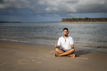 Naklejka na ściany i meble White man between 25 and 30 years old at the edge of the sea doing yoga.