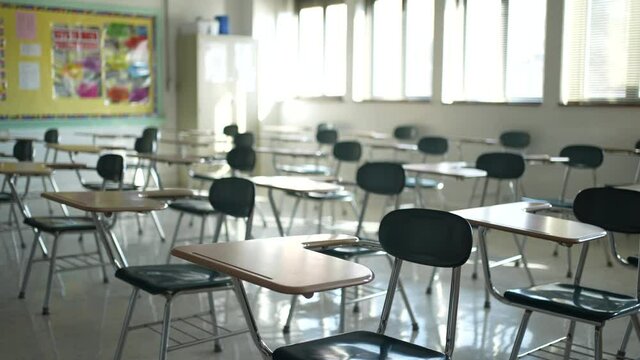 Desks in empty dark high, middle, or elementary school classroom with light coming through windows.