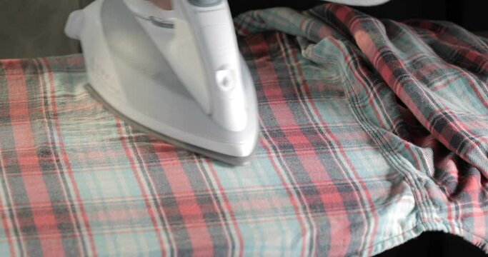 Male hands ironing clothes with iron on ironing board	