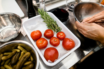 White tray with fresh red tomatoes and green springs of rosemary on kitchen table