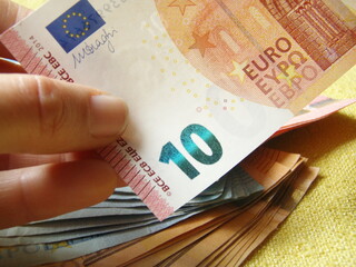 billete  de 10 euros sujetado con dedo y colocado encima de fajos de otros. colores naranjas y...
