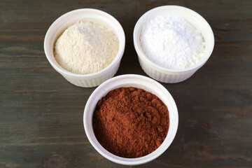 Obraz na płótnie Canvas Closeup a Bowl of Cocoa Powder with Blurry Bowl of Whole-wheat Flour and White Flour on Black Wooden Table
