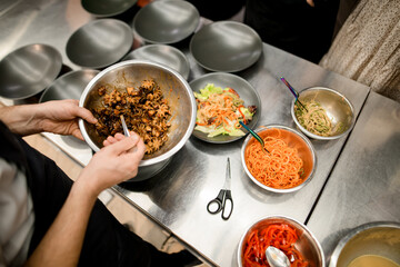hands of chef holds bowl with octopuses and bowls with other ingredients on the table