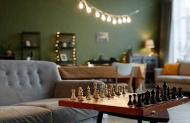 Cozy living room with pastel green walls, bright glowing lights and chess board on foreground