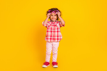 Photo of cute pretty school girl dressed checkered clothes arms heart spectacles smiling isolated yellow color background