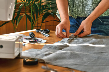 Woman is sketching pattern on a linen fabric Seamstress basting and sewing in a small studio...
