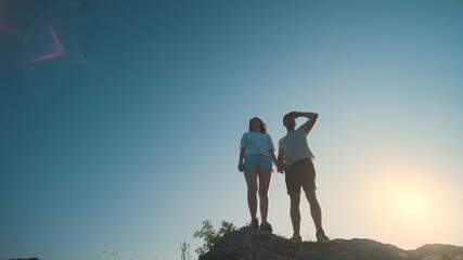 The young couple standing on a mountain top on a blue sky background