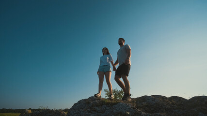 The young couple standing on a mountain top on a blue sky background