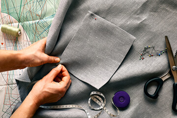 Woman is sketching pattern on a linen fabric Seamstress basting and sewing in a small studio...