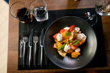 Selective focus on tasty salad in black plate on served table.