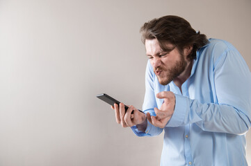 Aggressive young business man in blue shirt shouting into his mobile phone on grey background
