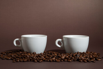 two cups of coffee on a pile of coffee beans on a brown background.