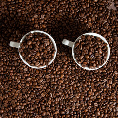 two cups of coffee on coffee beans on a brown background.